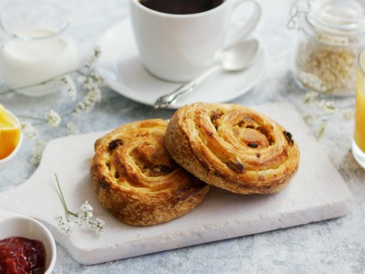 Served delicious breakfast meal with baked buns on wooden board on marble table with coffee and juice and jam